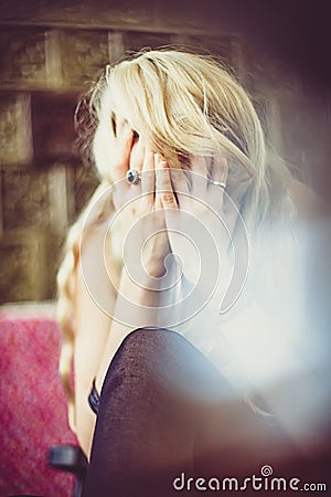 Sitting blonde woman crying and hiding her face Stock Photo