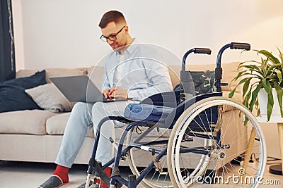 Sitting on sofa with laptop on legs. Disabled man in wheelchair is at home Stock Photo