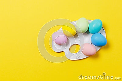 Six colorful pastel monophonic painted Easter eggs on drawing empty palette isolated on yellow background. Happy Easter Stock Photo