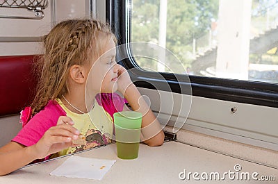 Six-year girl sitting on train at the table on outboard second-class carriage and enthusiastically looking out the window Stock Photo