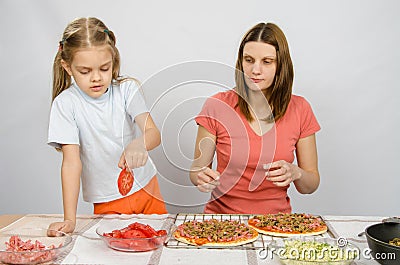 Six year old girl takes plate of cutting tomatoes for pizza under the supervision of mum Stock Photo