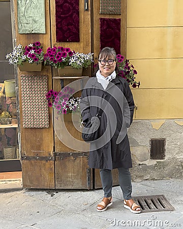 Sixty-five year-old female Korean tourist enjoying a sidewalk flower display in Pitigliano, Italy. Stock Photo