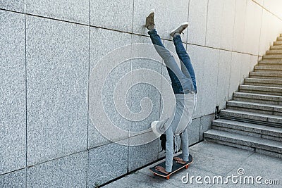 Skateboarder doing a handstand on skateboard against wall Stock Photo