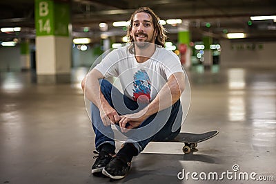 Skateboarder sitting on his skateboard in the underground garage Stock Photo