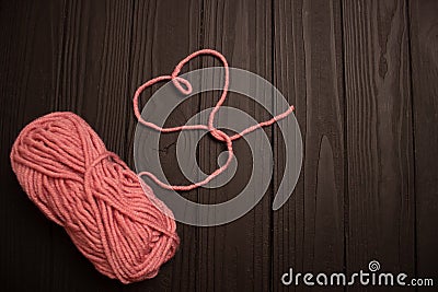 a skein of pink yarn and a heart of thread on a dark wooden background Stock Photo