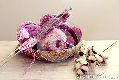 Skeins of multicolored yarn in purple tones, knitting needles on a decorative tray, a branch of cotton on a light table, gray Stock Photo