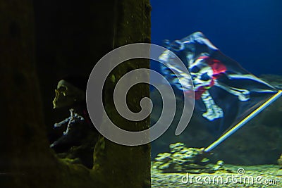 Skeleton of a dead pirate at the bottom of the ocean next to a waving pirate flag with crossbones and a skull. Adventure and Stock Photo