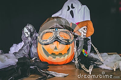 Skeleton, a ghost, a jack o lantern and fake spider webbing on top of a wooden table against a black background Stock Photo