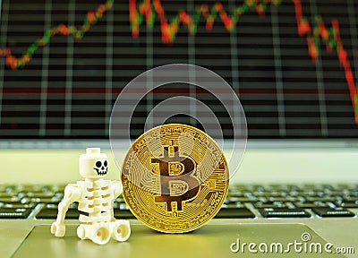 A skeleton and a gold bitcoin standing on a notepad of a notebook computer with a stock graph in the background Editorial Stock Photo