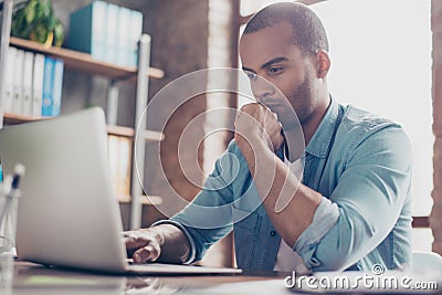 Skeptic young afro freelancer is making decision sitting at the office in casual smart, analyzing the data in the computer Stock Photo