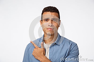 Skeptical, disappointed and doubtful handsome young man, frowning and grimacing from dislike, indecisive pointing left Stock Photo