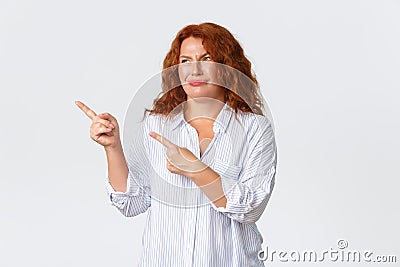Skeptical and disappointed redhead middle-aged woman, mother dislike promo banner, pointing and looking upper left Stock Photo