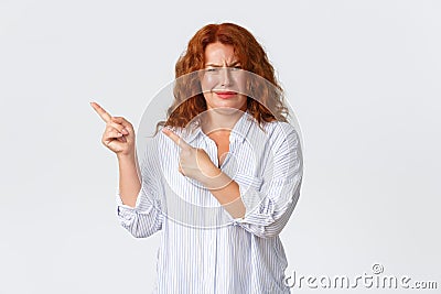 Skeptical and judgemental redhead middle-aged woman pointing upper left corner and grimacing from some nonsense Stock Photo