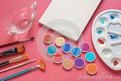 Sketchbook, palette, paintbrushes and watercolor paints on pink background Stock Photo