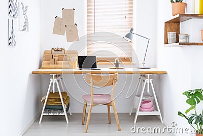Sketchbooks and an open laptop on a wooden desk in a white, home office interior of a fashion designer. Real photo. Stock Photo