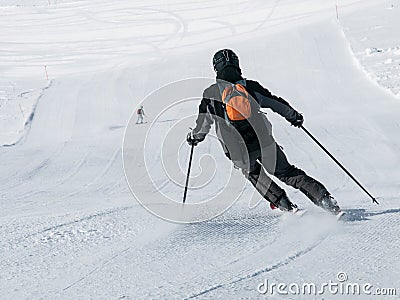 Skier in black downhill skiing on a ski slope. View from back Stock Photo
