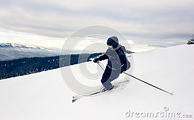 Skier inclining turning on snow-capped mountain peak. Extreme skiing concept. Mountains view. Grey sky on background. Stock Photo