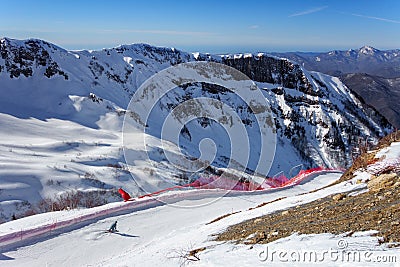 Skier riding along snowy ski slope of Gorky Gorod winter mountain ski resort on blue sky and snowy Caucasus peaks scenic Stock Photo