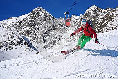 Skier skiing downhill in high mountains against cable lift Stock Photo