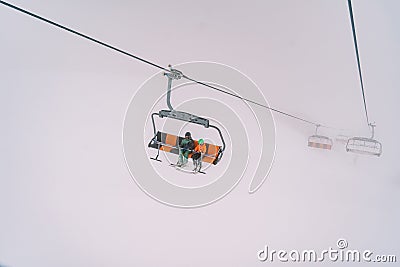 Skiers on a chairlift ascend a mountain through thick fog Stock Photo