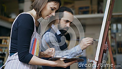 Skilled artist man teaching young woman painting on easel at art school studio - creativity, education and art people Stock Photo