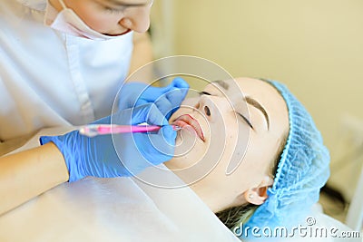 Skilled cosmetologist shaping lips with pencil for young woman before microblading. Stock Photo