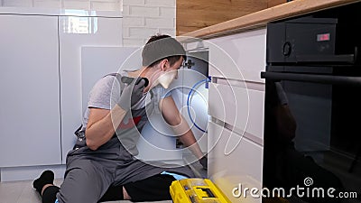 Skilled craftsman with flashlight examines pipes under sink Stock Photo