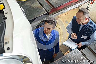 Skilled mechanics in coveralls working under lifted up car Stock Photo