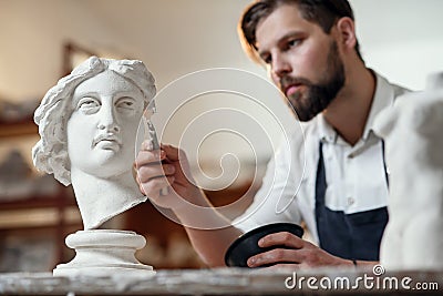 Skillful sculptor makes professional restauration of gypsum sculpture of woman`s head at the creative workshop. Stock Photo