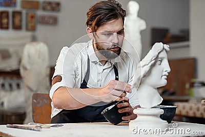 Skillful sculptor makes professional restauration of gypsum sculpture of woman`s head at the creative workshop. Stock Photo