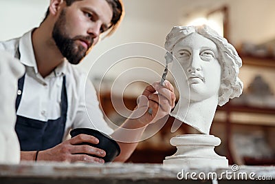 Skillful sculptor makes professional restauration of gypsum sculpture of woman`s head at the creative workshop. Stock Photo