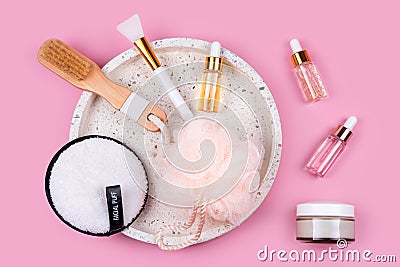 Skin care essence glass bottles, facial sponge, creme, spa brush and washcloths on marble cosmetic tray on pink background. Stock Photo