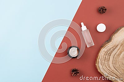 Skin care products. Open cream jar, serum with peptides, wooden cross section cut, pine cones on brown and blue surface Stock Photo