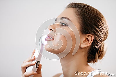 Skin Care. Side portrait of the charming healthy fresh woman with natural make-up using the electric facial massager at Stock Photo