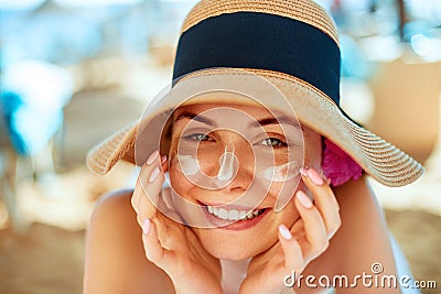 Skincare. Beauty Concept. Young pretty woman applying sun cream and touch own face. Female in hat smear sunscreen lotion on skin. Stock Photo