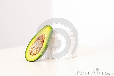 Skincare with natural cosmetics. White cosmetic jar of cream with half of the avocado near against white background Stock Photo