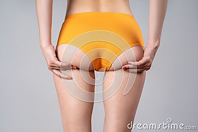 Skinny female buttocks in yellow panties on gray background, anti cellulite massage Stock Photo