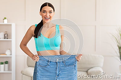 Skinny Woman Comparing Oversize Jeans After Weight Loss At Home Stock Photo