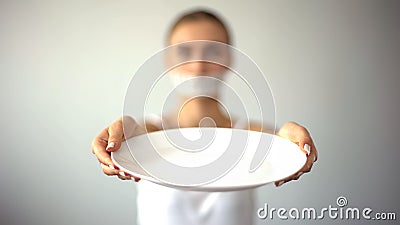 Skinny woman with taped mouth showing empty plate, concept of fasting, hunger Stock Photo