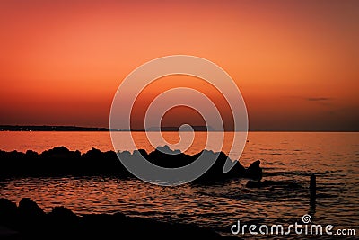 Skyline after sundown. Scenery of orange sky with rock silhouette and ocean waves. Orange sunset at shoreline photography. Stock Photo