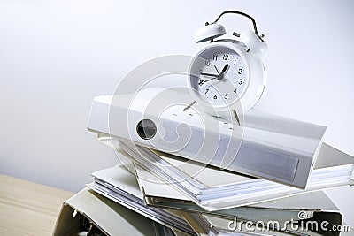 Slanted stack of ring binders and a white alarm clock on top reminding to the deadline, business concept of bureaucracy, Stock Photo