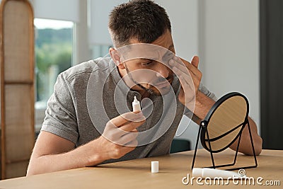 Sleep deprived man covering up dark circles with concealer near mirror at home Stock Photo