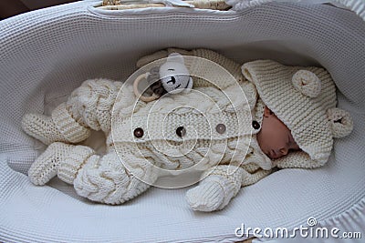 Sleeping beautiful 2 month old baby girl in a white knitted suit lies in her white crib Stock Photo