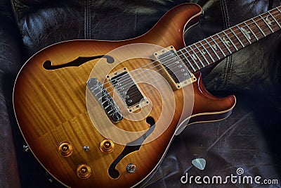 `Sleeping Beauty` hollowbody acoustic electric guitar in leather chair with pick Stock Photo