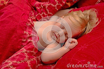 Sleeping blond baby on red bedding, close-up Stock Photo