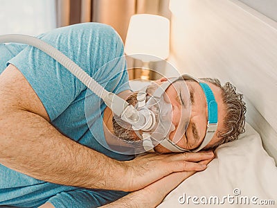 Sleeping man with chronic breathing issues considers using CPAP machine in bed. Stock Photo