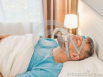 Sleeping man with chronic breathing issues considers using CPAP machine in bed. Stock Photo