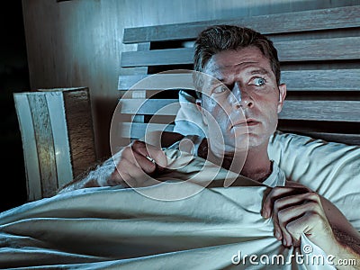 Sleepless young man lying in bed stressed and scared suffering nightmare and horror bad dream grabbing duvet frightened and parano Stock Photo