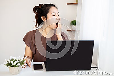 Sleepy Asian woman worker yawning and tired working late from home office Stock Photo