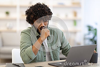 Sleepy dark-skinned guy sitting at workdesk in front of laptop Stock Photo